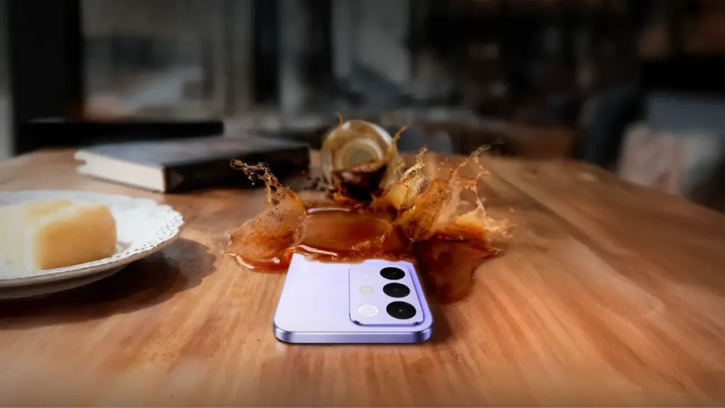 Realme C85 5G smartphone demonstrating spill-resistant design with coffee splashing on a wooden table.